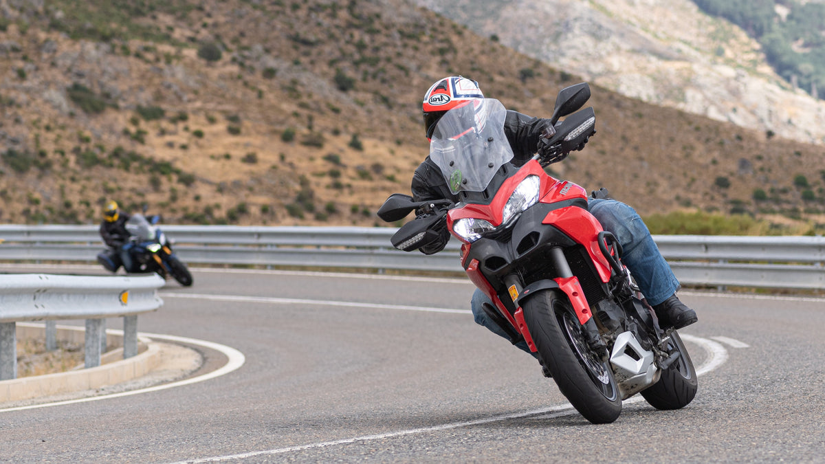 Motorcyclist on a red motorcycle on a winding road with mountains in the background